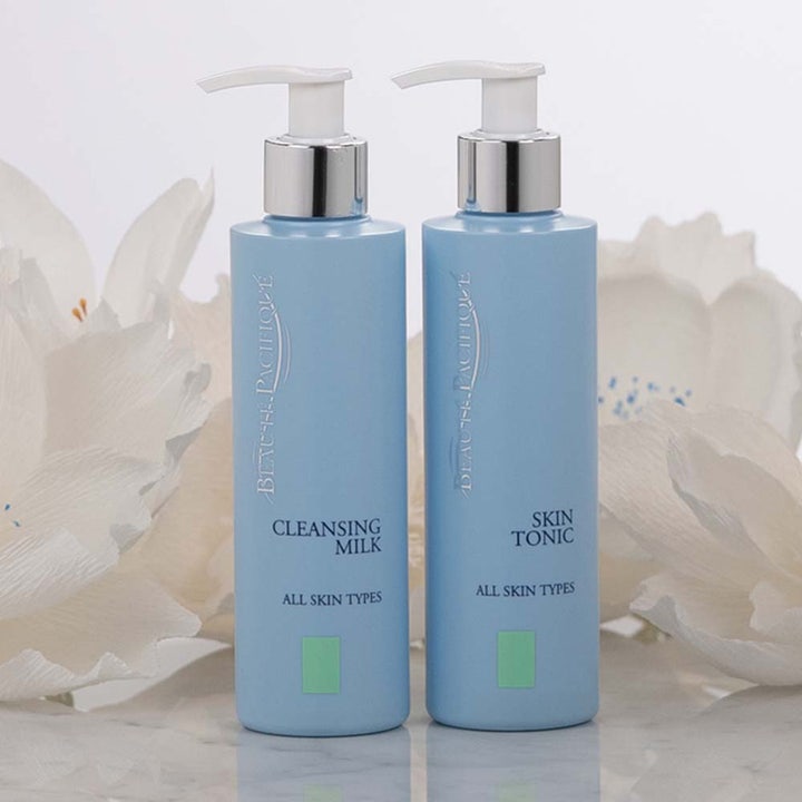 Beauté Pacifique Cleansing Milk 200 ml daglig återfuktande ansiktsrengöring i ljusblå pumpflaska bredvid vita blommor.