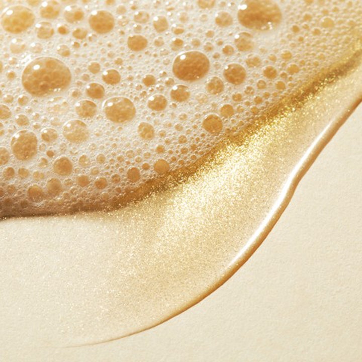 Nuxe Prodigieux Shower Oil 200 ml duscholja med guldskimmer visar en skimrande gyllene textur och mjukt vitt skum.
