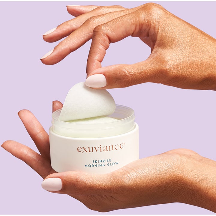Exuviance SkinRise Morning Glow 36 st lysterivande pads i vit burk där en hand lyfter upp en pad.