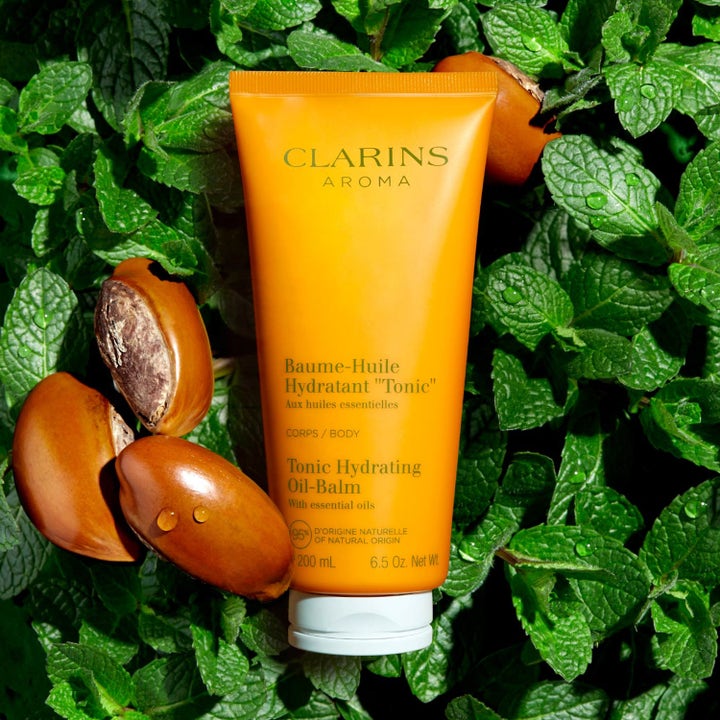 Clarins Hydrating Toning Body Balm 200 ml gul tub ger fukt omgiven av gröna blad och bruna frön