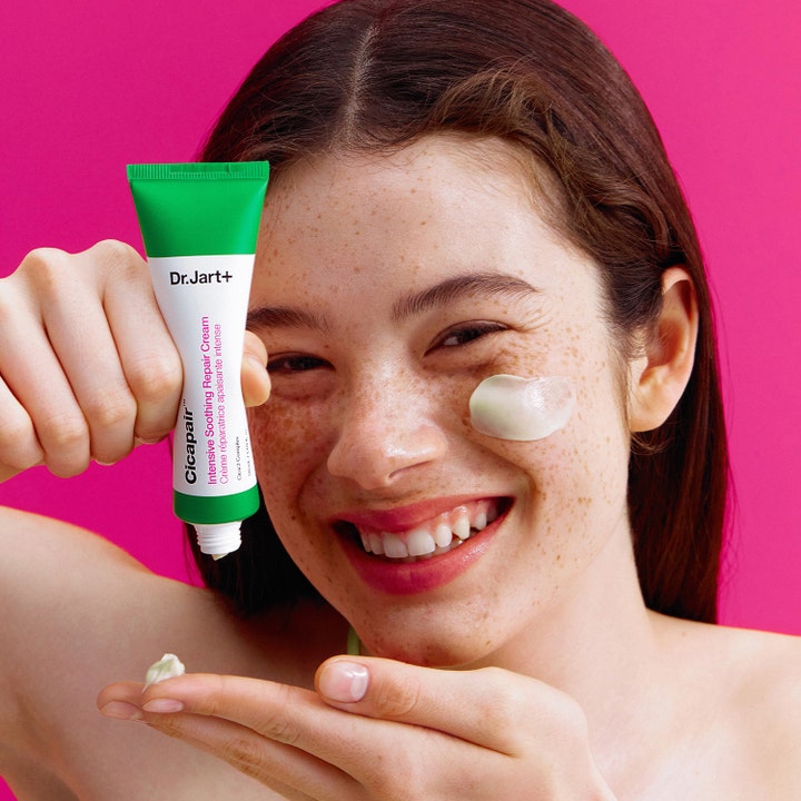 Dr.Jart+ Cicapair Intensive Soothing Repair Cream 50 ml cica lugnande ansiktskräm på tub som appliceras på en leende kvinnas kind.