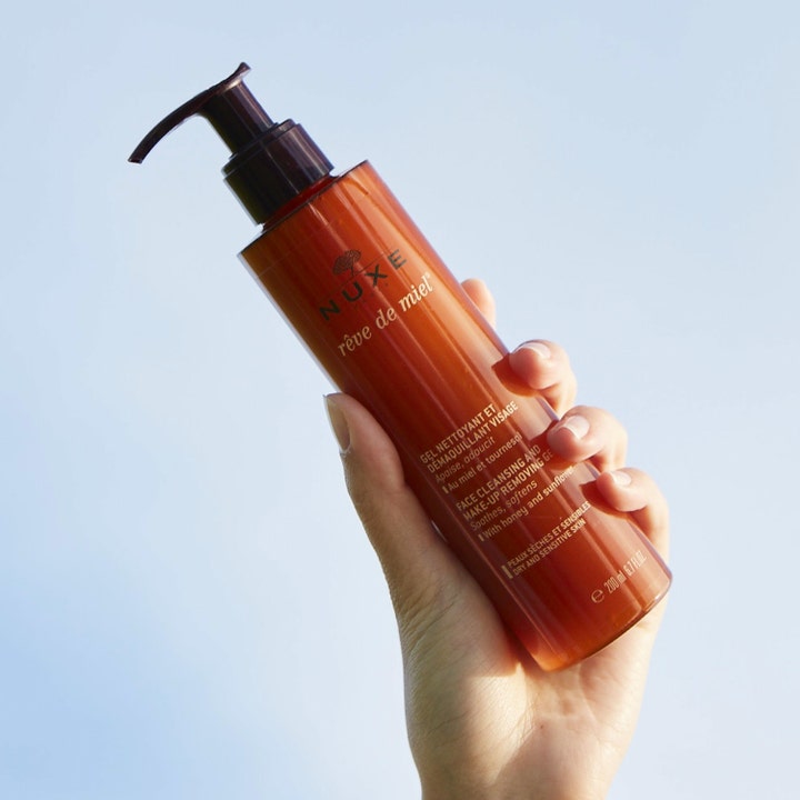 Nuxe Rêve de Miel 200 ml lugnande rengöringsgel i bärnstensfärgad pumpflaska som hålls upp mot en klarblå himmel.