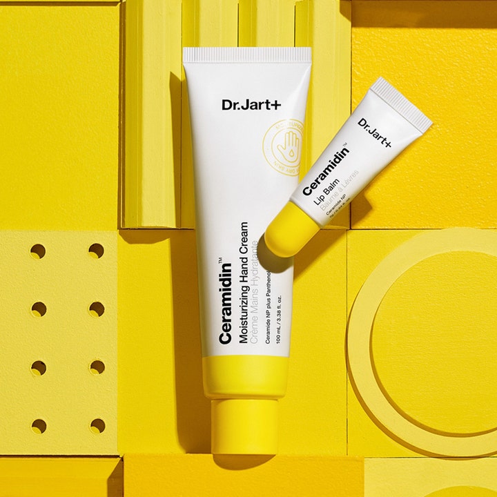 Dr.Jart+ Ceramidin Moisturizing Hand Cream 100 ml återfuktande handkräm i vit tub bredvid läppbalsam på gul dekor