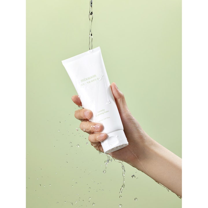 Mixsoon Centella Cleansing Foam Cleanser 150 ml centella ansiktstvätt i vit tub som sköljs med vatten mot grön bakgrund.