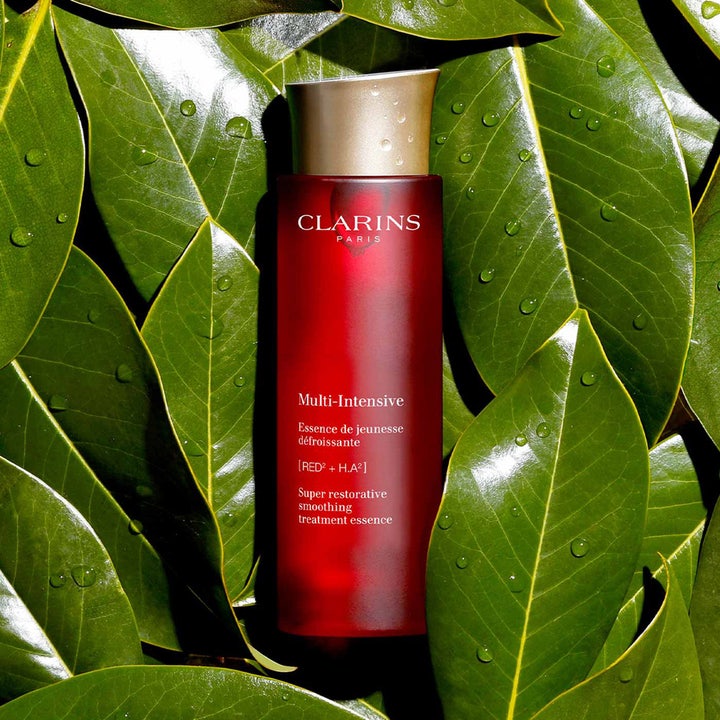 Clarins Super Restorative Treatment Essence 200 ml anti-rynk essens i röd flaska på gröna blad med vattendroppar.