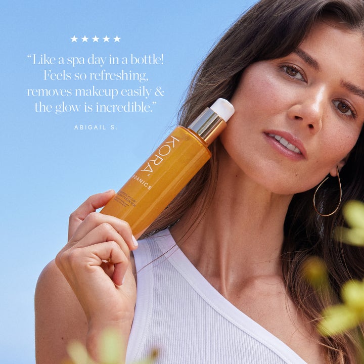 KORA Organics Turmeric Glow Foaming Cleanser 150 ml lystergivande gurkmeja ansiktsrengöring som hålls mot en kvinnas kind.