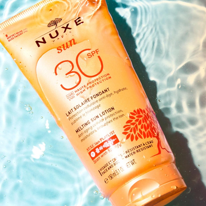 Nuxe Sun Delicious Lotion 150 ml solkräm för ansiktet och kropp i orange tub som flyter i glittrande vatten.