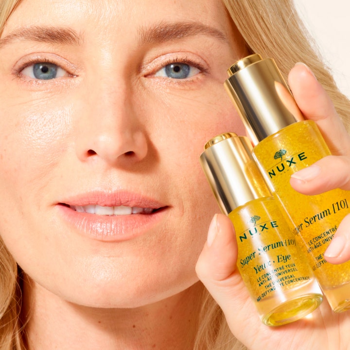 Nuxe Super Serum [10] Eye 15 ml anti-rynk ögonserum med guldiga mikropärlor som hålls upp av en kvinna.