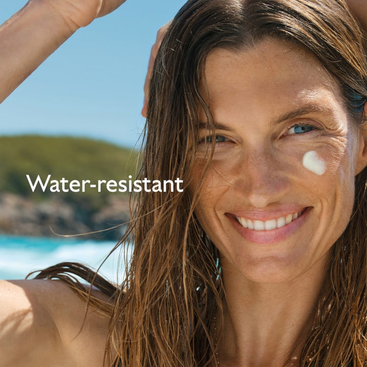 Caudalie Vinosun High Protection Glow Oil 150 ml water-resistant solskydd ger lyster på en leende kvinna vid stranden