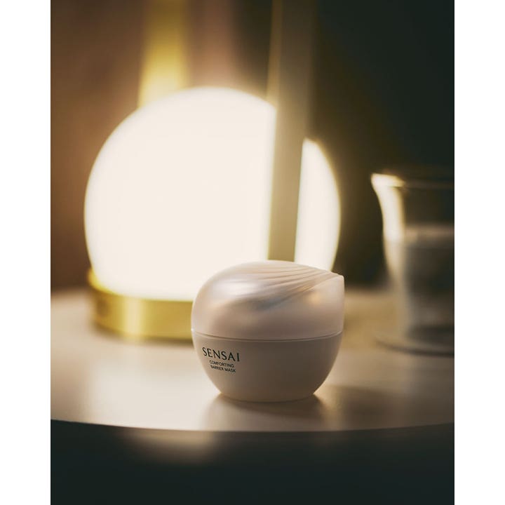 Sensai Comforting Barrier Mask 60 ml lugnande ansiktsmask i vit rund burk placerad i mjukt ljus