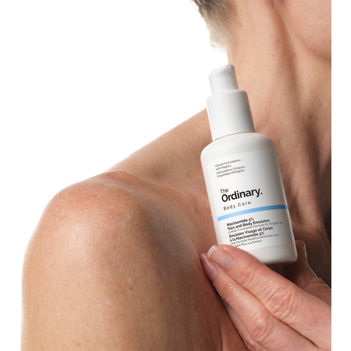The Ordinary Niacinamide 5% Face & Body Emulsion 100 ml mot ojämn hudton i vit pumpflaska som hålls mot en axel.