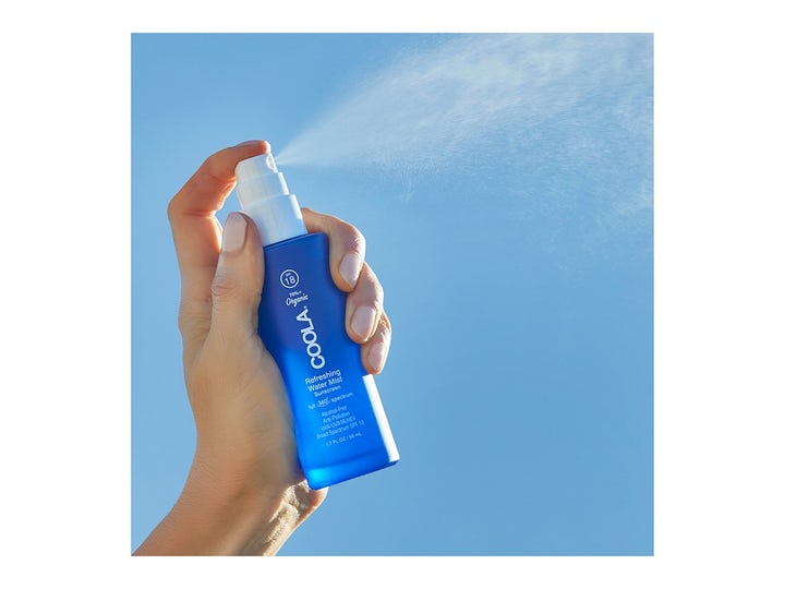 COOLA Refreshing Water Mist 50 ml solskydd ansikte spray i blå flaska som sprayas mot en klarblå himmel.