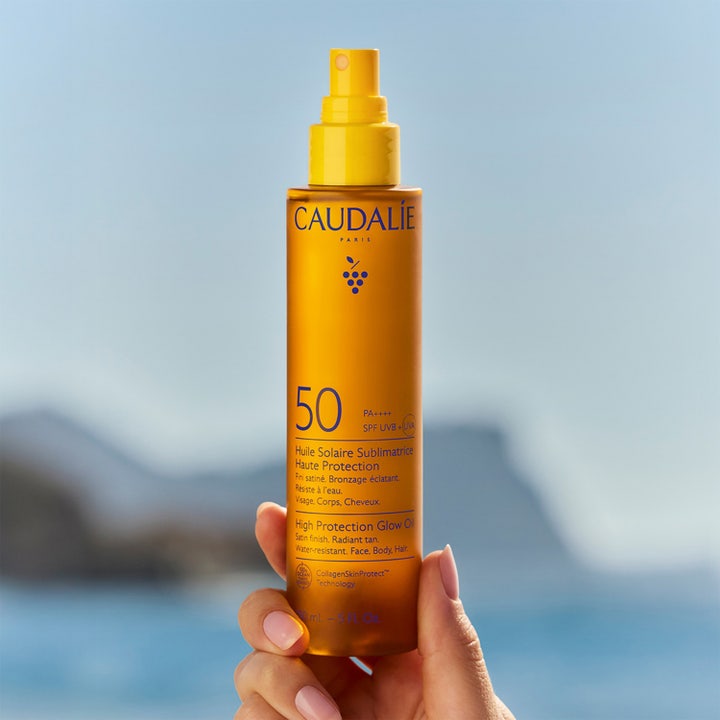 Caudalie Vinosun High Protection Glow Oil 150 ml solskydd som ger lyster i orange sprayflaska framför havet.