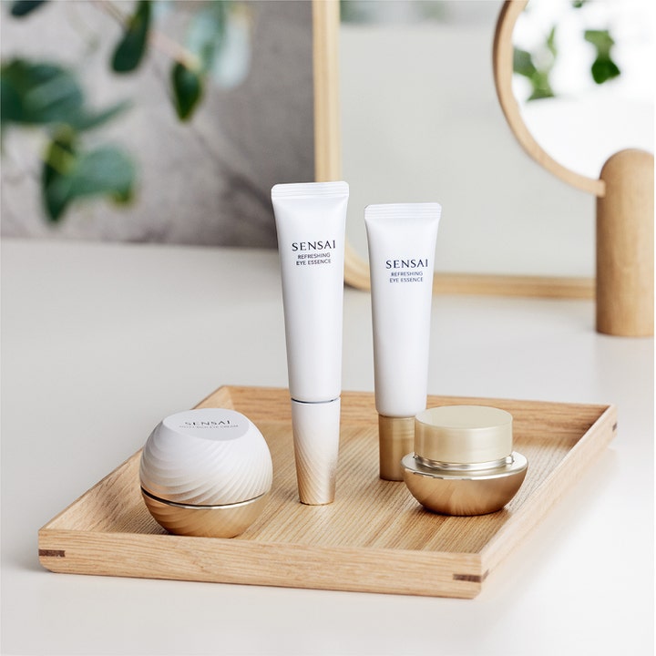 Sensai Total Eye Treatment 35 ml återfuktande ögonkräm mot mörka ringar i vita tuber och guldiga burkar på en träbricka