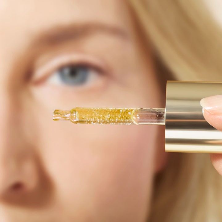 Nuxe Super Serum [10] Eye 15 ml anti-rynk ögonserum med gyllene mikropärlor i pipett framför ett öga.