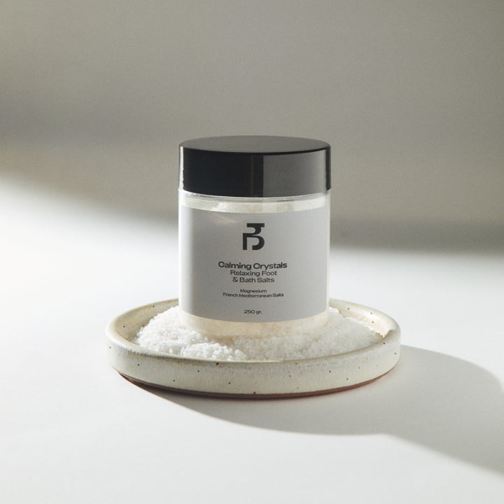 Bodyologist Calming Crystals 250 g lugnande badsalt i genomskinlig burk på ett keramikfat fyllt med vita kristaller