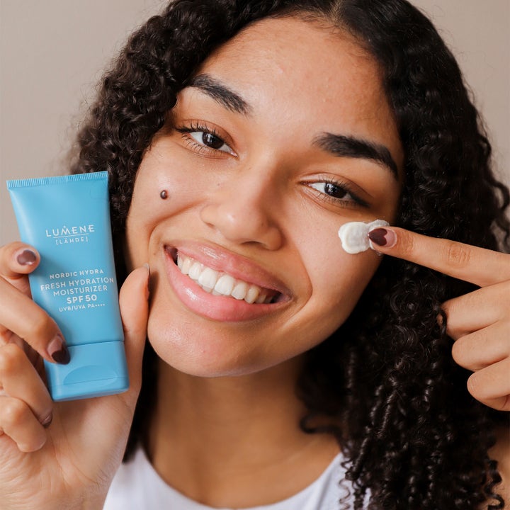Lumene Nordic Hydra 50 ml återfuktande dagkräm för ansiktet med spf 50 som en kvinna applicerar från en blå tub.