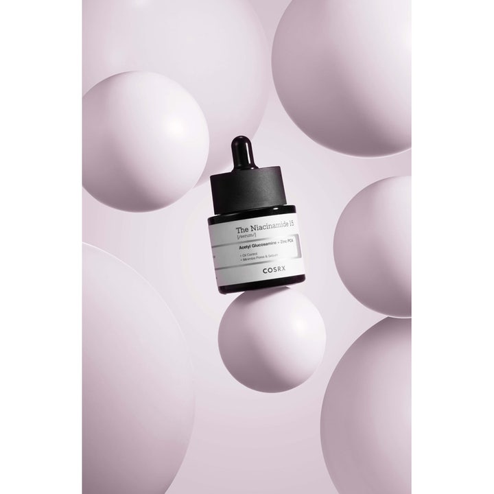 COSRX The Niacinamide 15 Serum 20 ml för fet hy i mörk glasflaska omgiven av ljuslila sfärer.
