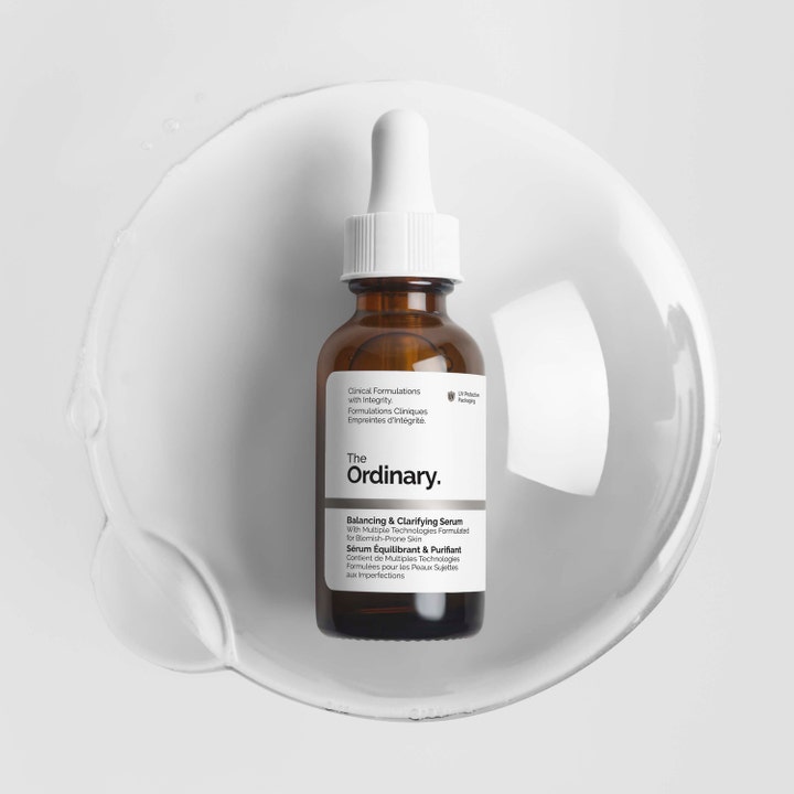 The Ordinary Balancing & Clarifying Serum 30 ml balanserande ansiktsserum i brun glasflaska i en cirkel av klar vätska