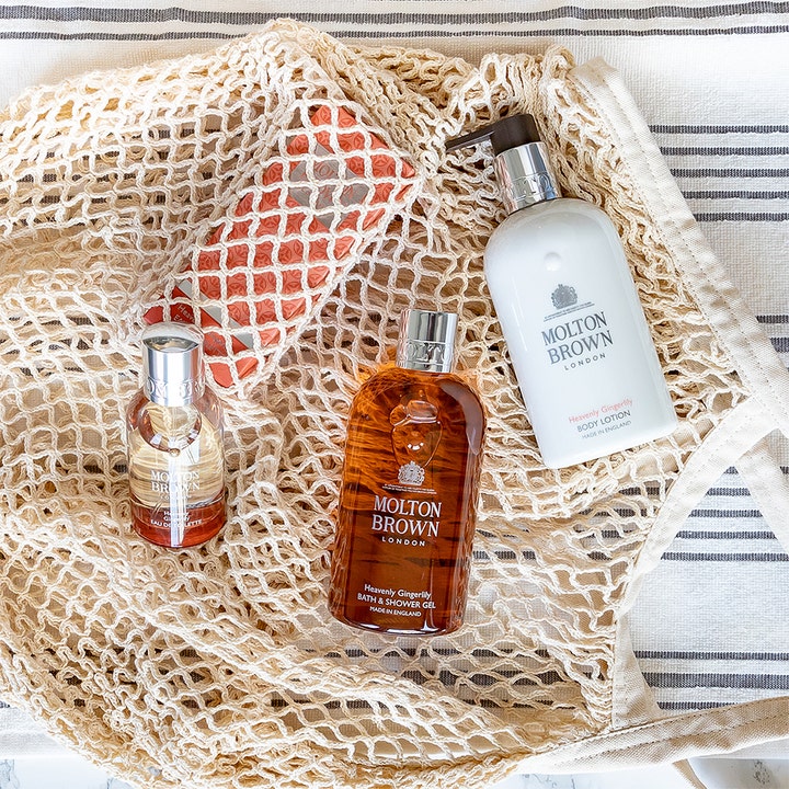 Molton Brown Heavenly Gingerlily 300 ml aromaterapi duschtvål i bärnstensfärgad flaska i en beige nätkasse.