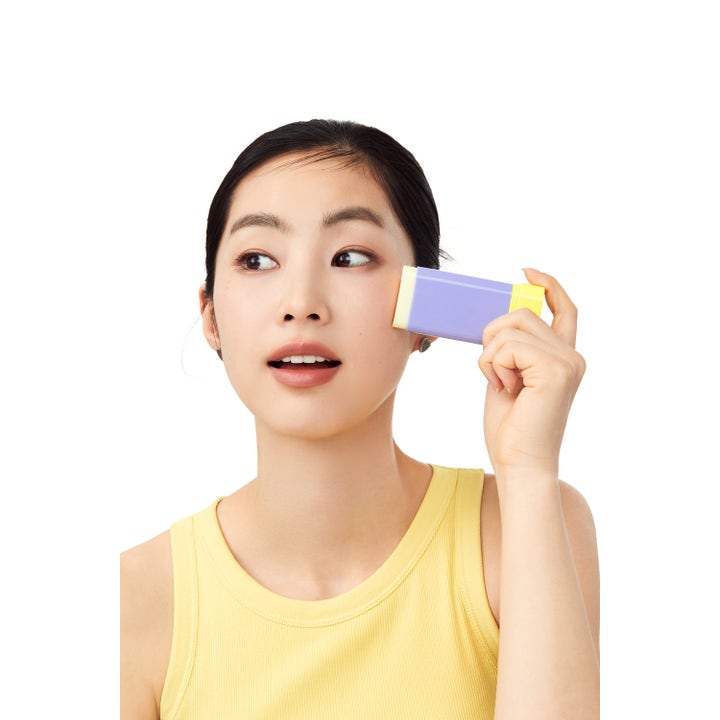By Wishtrend Pore Smoothing Bakuchiol Sun Stick 18 g lila solstift som en kvinna applicerar direkt mot kinden.