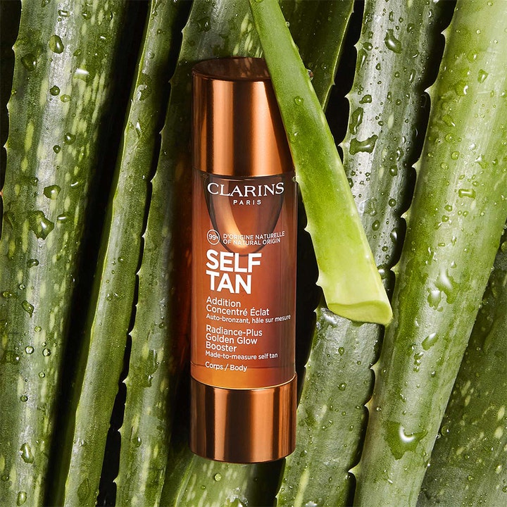 Clarins Radiance-Plus Golden Glow Booster Body 30 ml tanning drops i bronsfärgad flaska bland gröna aloe vera-blad.