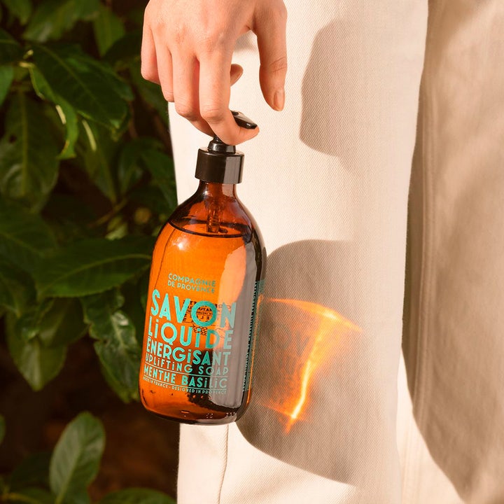 Compagnie de Provence Liquid Marseille Soap 495 ml energigivande lyxig handtvål i brun glasflaska som hålls i en hand.