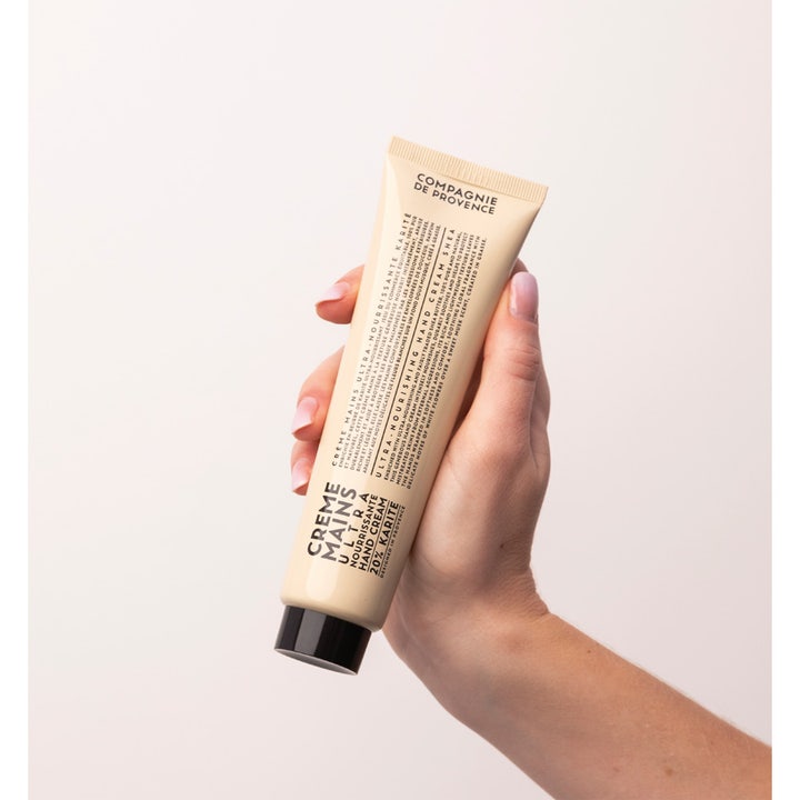 Compagnie de Provence handkräm 20% karité 100 ml ger näring i en beige tub som hålls i en hand.