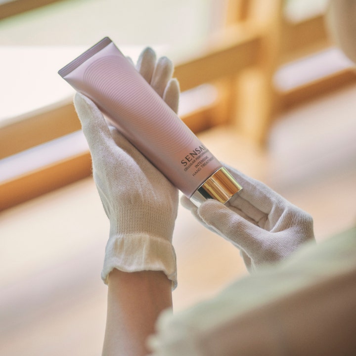 Sensai Cellular Performance handkräm 100 ml återfuktande anti-aging i händerna på en person med vita bomullsvantar