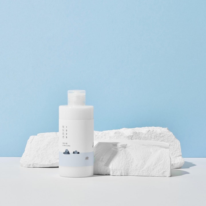 Round Lab 1025 Dokdo Lotion 400 ml återfuktande K-beauty hudvård i vit flaska vid vita stenar och blå bakgrund