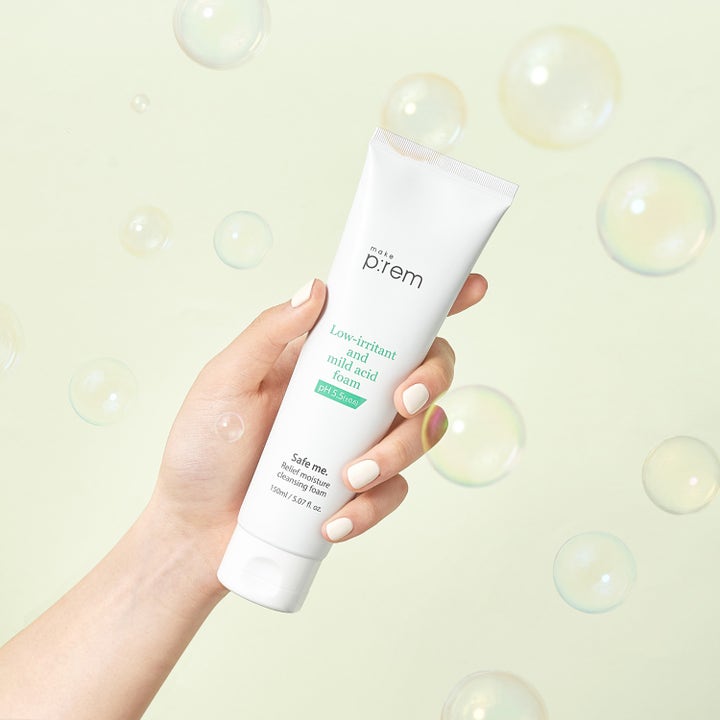 Make Prem Safe Me. Relief Moisture Cleansing Foam 150 ml i vit tub hålls av en hand mot en bakgrund av bubblor