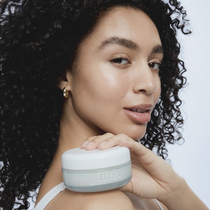 RMS Beauty Coconut Clean Cleansing Balm 100 g clean beauty cleansing balm i glasburk som hålls av en modell.