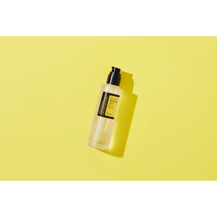 COSRX Advanced Snail 96 Essence 100 ml återfuktande serum med snigelslem i genomskinlig pumpflaska mot gul bakgrund