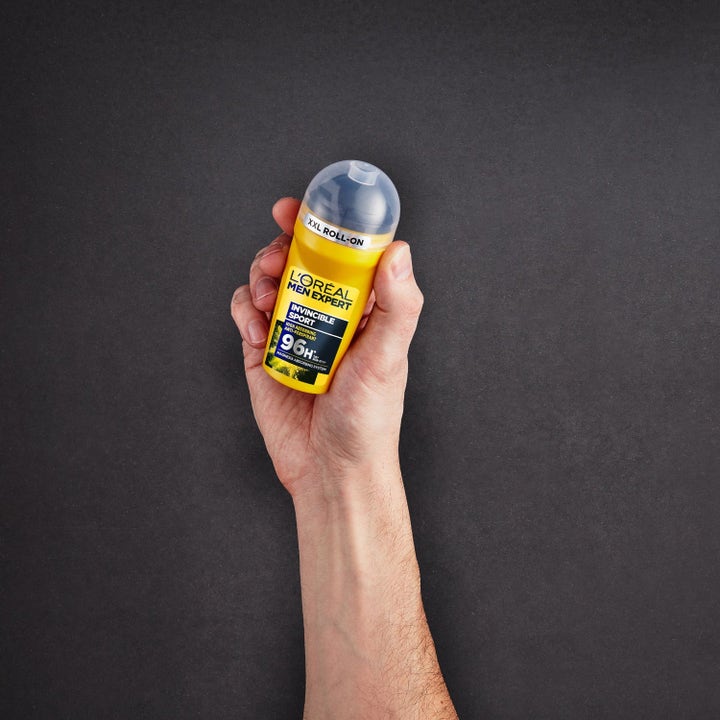 L'Oréal Paris Men Expert Invincible Sport 50 ml rollon deo i gul förpackning som hålls i en hand mot mörk bakgrund.