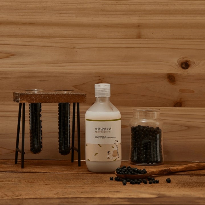Round Lab Soybean Nourishing Toner 300 ml närande toner i flaska omgiven av svarta sojabönor mot träbakgrund