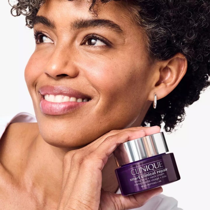 Clinique Smart Clinical Repair Lifting Face + Neck Cream 75 ml uppstramande dagkräm i lila burk som hålls av en kvinna