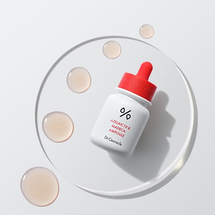 Dr. Ceuracle Azelaic 10 & Madeca Ampoule 30 ml serum i vit flaska med röd kork och ljusrosa droppar på en glasplatta