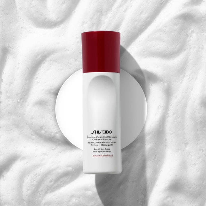Shiseido Defend Cleansing Microfoam 180 ml rengöringsmousse ansikte i vit flaska med rött lock mot ett mjukt vitt skum