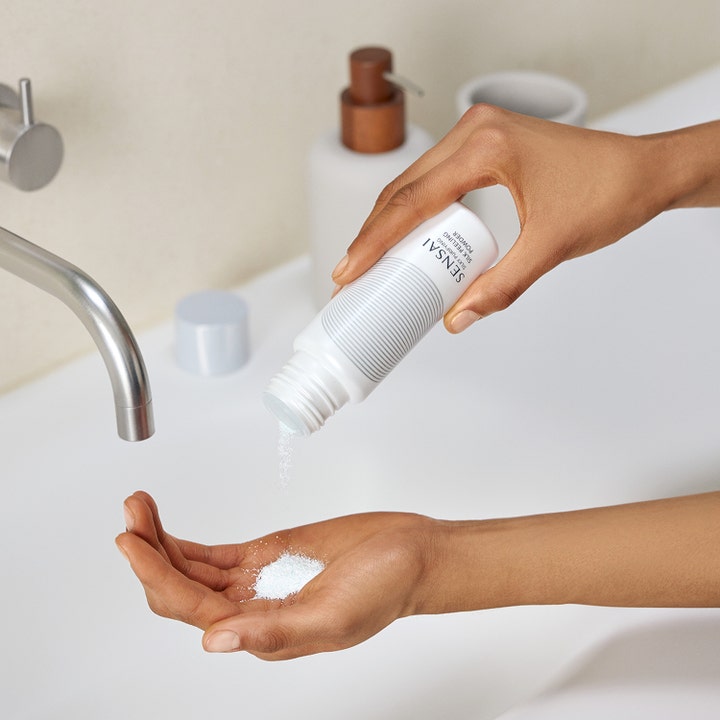 Sensai Silky Purifying Silk Peeling Powder 40 g enzympeeling ansikte som hälls ur vit flaska i en öppen handflata.