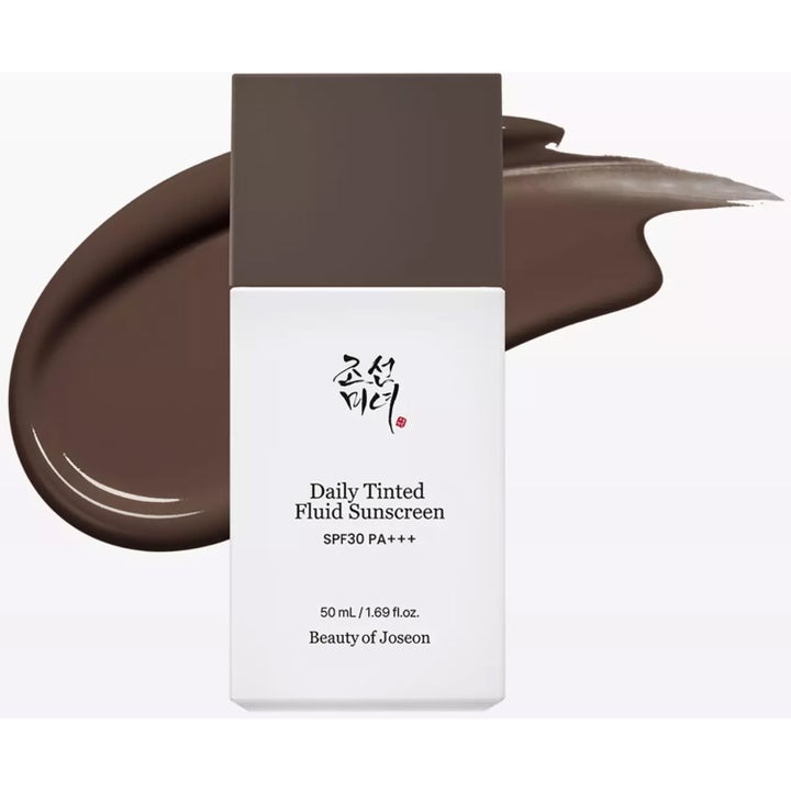 Beauty of Joseon Daily Tinted Fluid Sunscreen 50 ml tonat solskydd i vit flaska framför ett mörkbrunt krämigt svep.