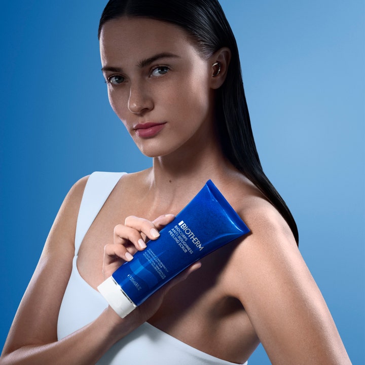 Biotherm Biocorps Body Scrub 200 ml exfolierande peeling för mjuk hy i blå tub som hålls av en kvinna.