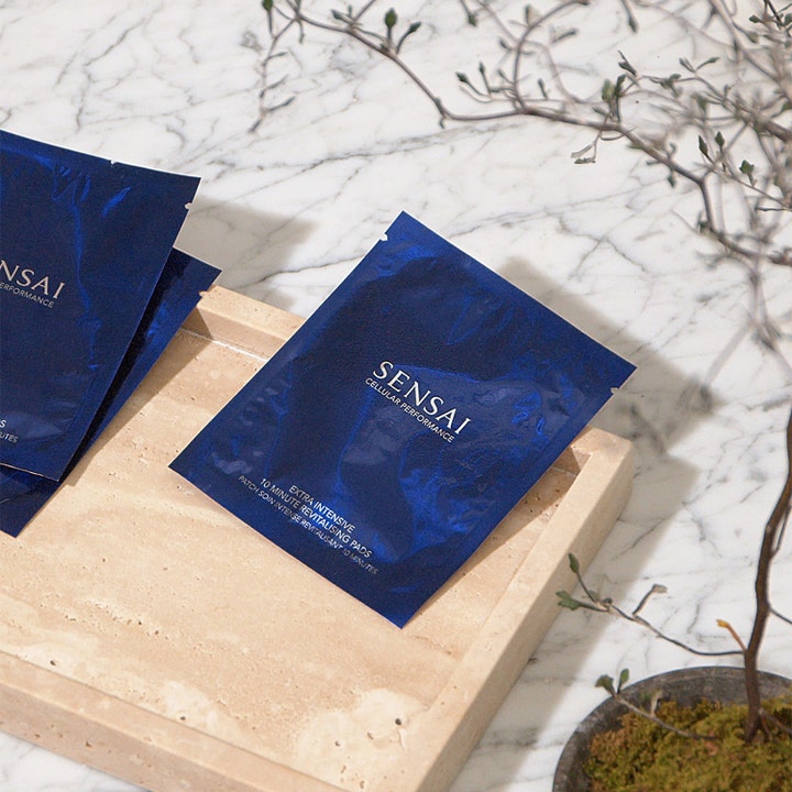 Sensai Cellular Performance 10 Minutes Revitalizing Pads 60 g ger revitalisering i mörkblå kuvert på en ljus stenbricka.