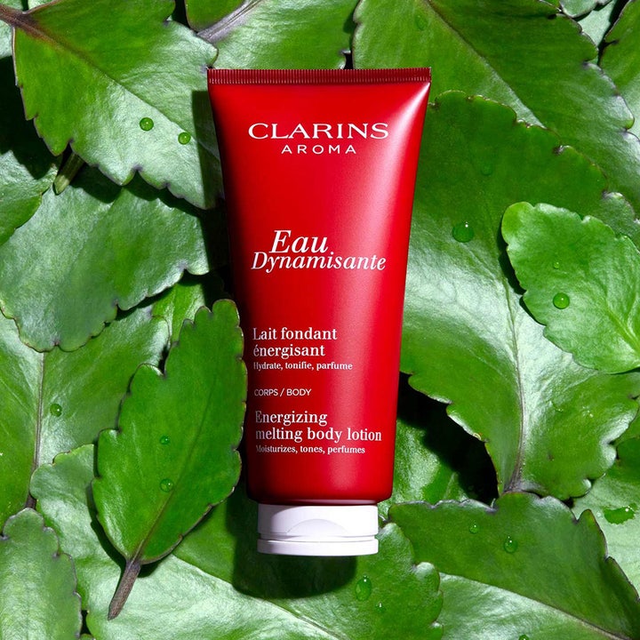 Clarins Eau Dynamisante 200 ml energigivande body lotion i röd tub placerad på gröna blad.