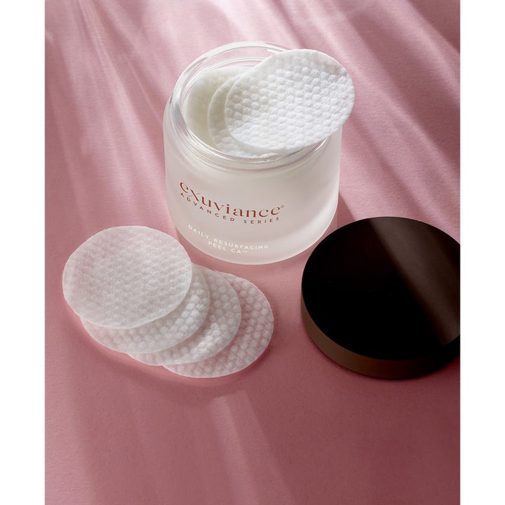 Exuviance Daily Resurfacing Peel 58 ml exfolierande peeling pads i öppen burk av frostat glas på rosa yta.