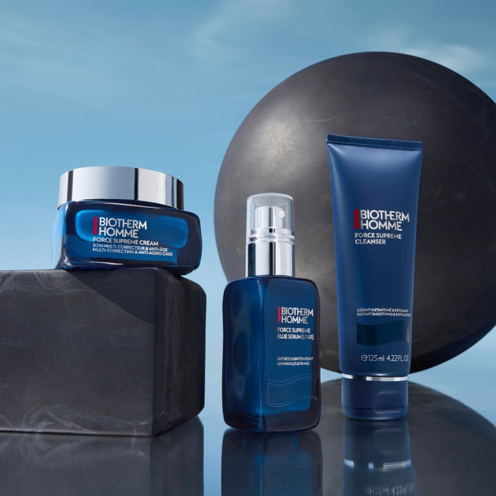 Biotherm Homme Force Supreme Blue Serum 60 ml och hudvårdsserie i blå förpackningar mot mörka stenar.