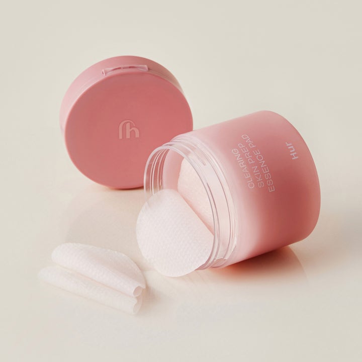 House of Hur Clearing Skin Prep Essence Pad 140 ml ger klar hud med vita rondeller i en öppen rosa frostad burk.
