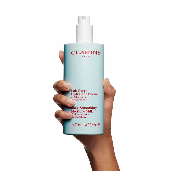 Clarins Hydrating Body-Smoothing Moisture Milk 400 ml återfuktande body lotion i ljusblå pumpflaska som hålls i en hand.