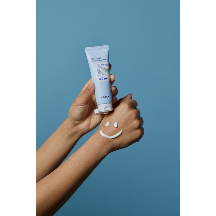 COSRX Ultra-Light Invisible Sunscreen 50 ml återfuktande solkräm med vit kräm formad som en smiley på en hand.