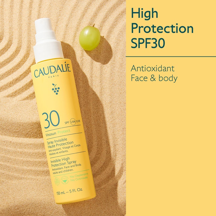 Caudalie Vinosun High Protection Spray SPF30 150 ml antioxidant solskydd spray i gul flaska på sand med en grön druva
