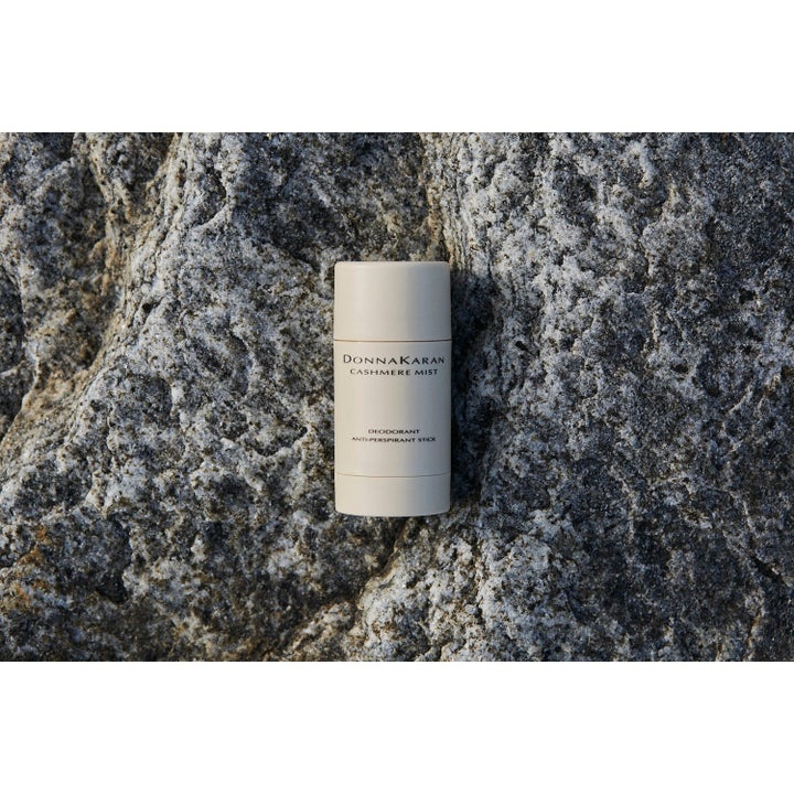 DKNY Cashmere Mist Deostick hudvård i beige förpackning som ger fräschör mot en rustik grå stenbakgrund.